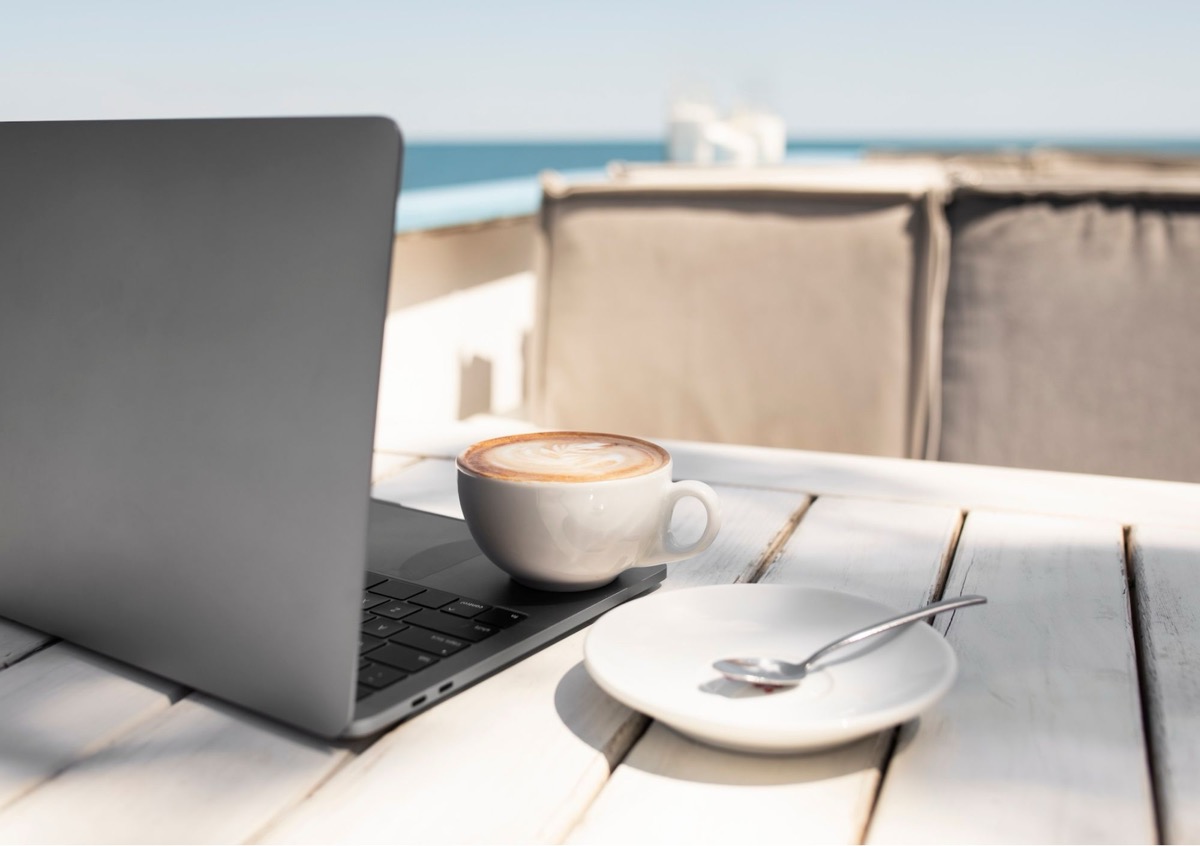 Eine Tasse Kaffee und ein Laptop an einem hellen Tisch am Meer